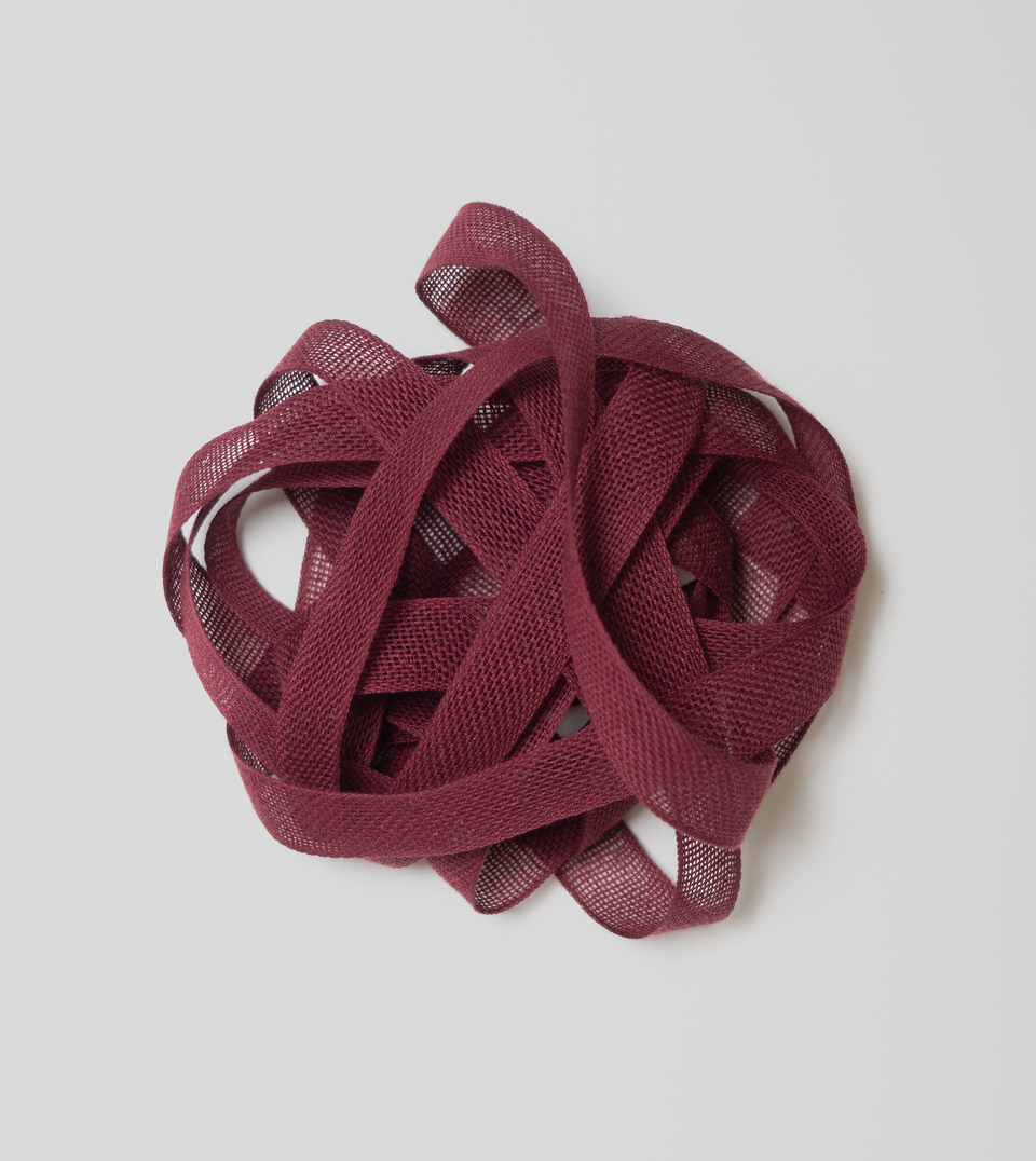 Wine-coloured loose-weave cotton ribbon on a light grey background. Studio Carta